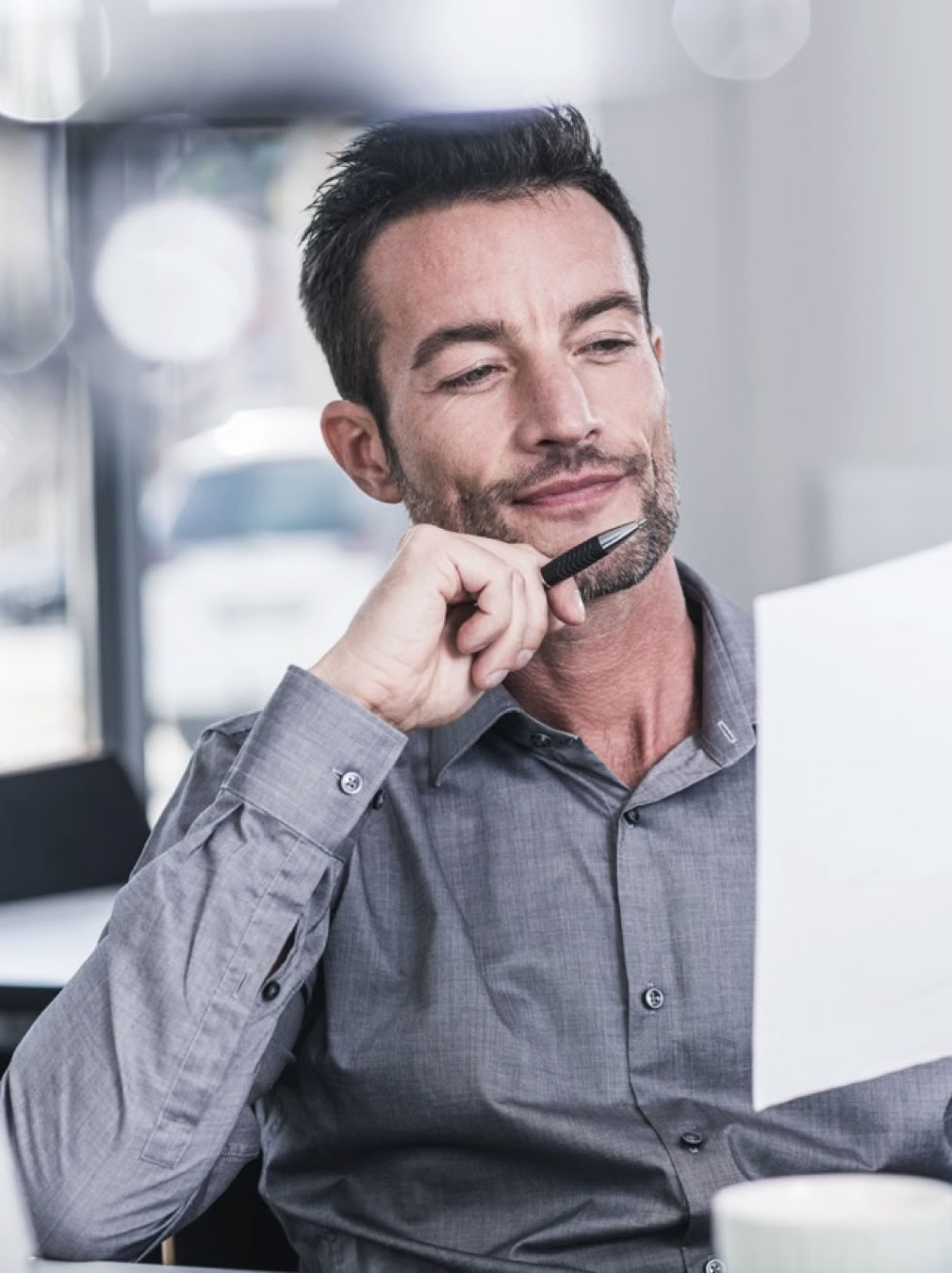 Man sat at desk with pen in hand and reading a sheet of paper